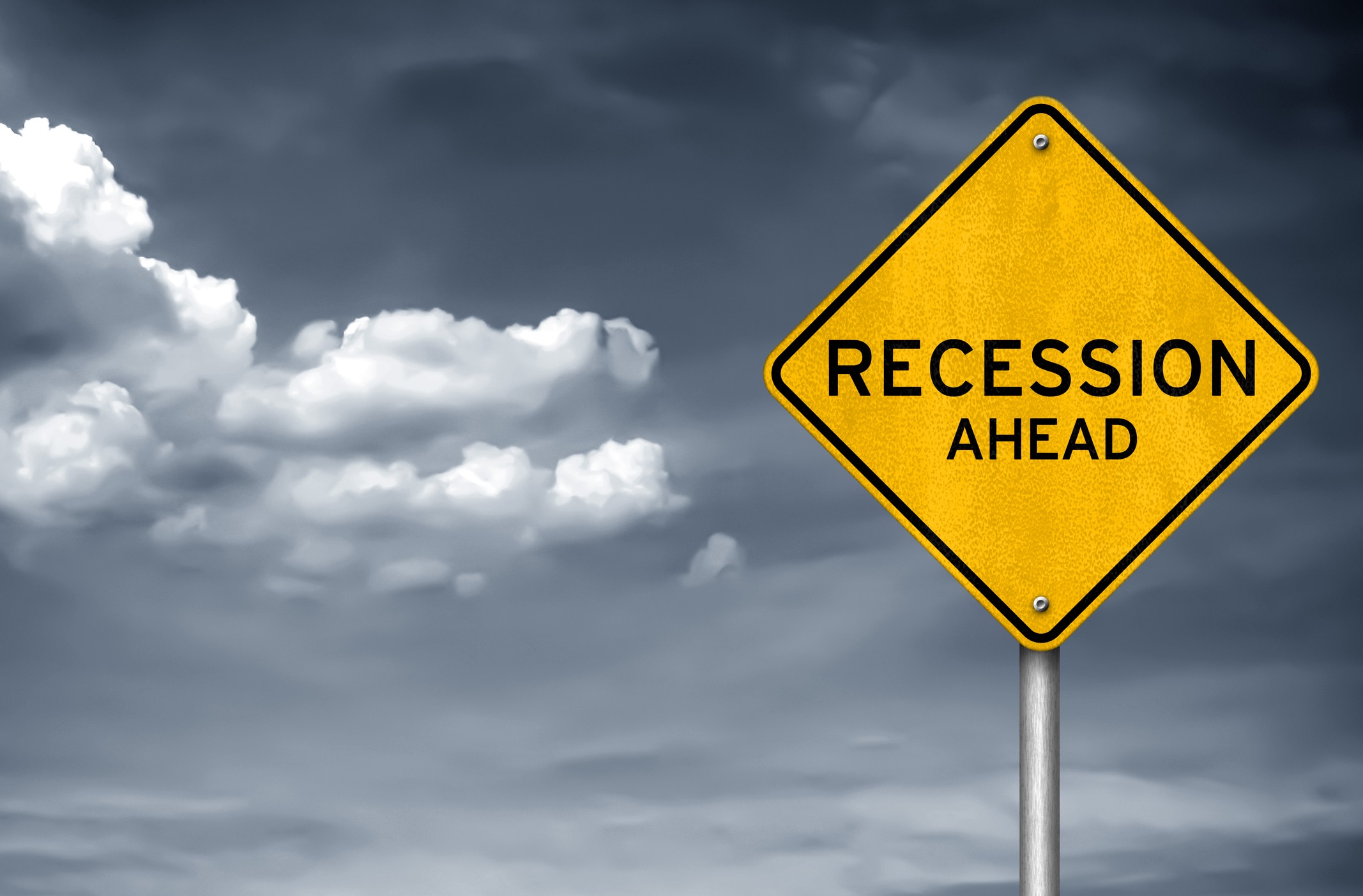 A yellow road sign warns "Recession Ahead" amidst a backdrop of storm clouds for self-fulfilling prophecy of recession blog.