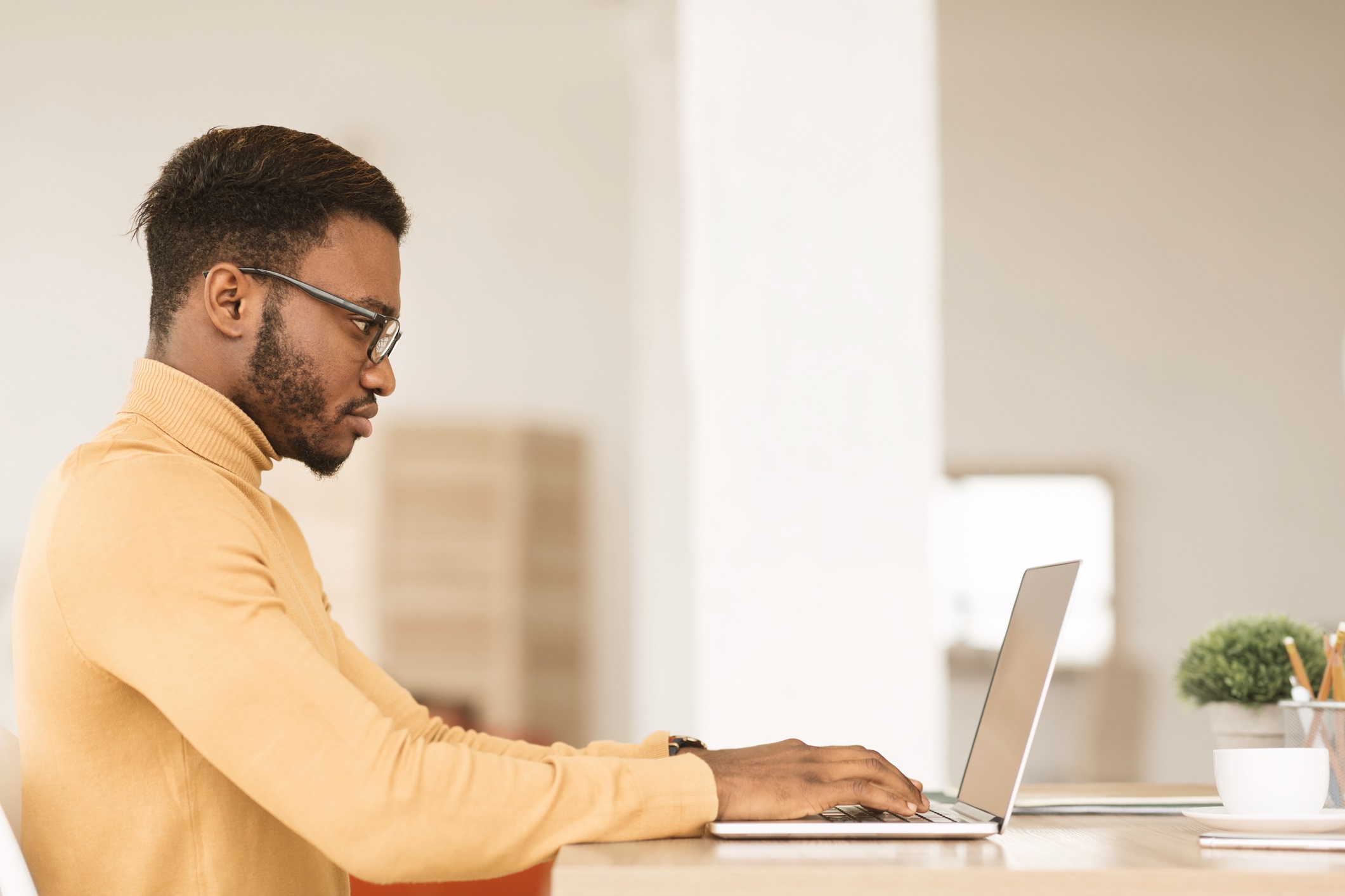 A black man wearing glasses and a yellow turtleneck works on his laptop for "Populating Your Google Business Profile" blog.