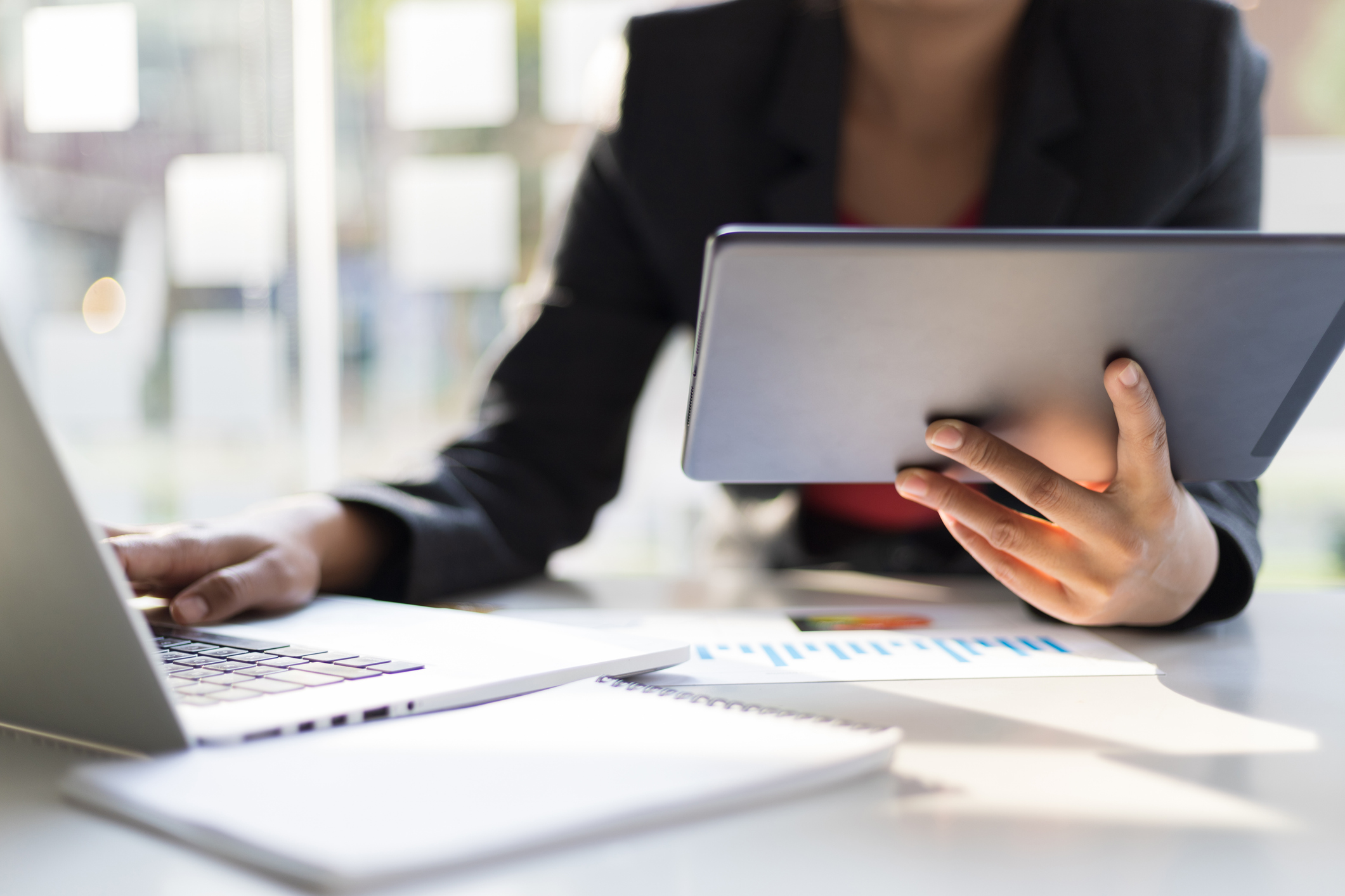 Business man holding tablet working on laptop and analyzing business plan. A business woman holds a tablet and simultaneously works on a laptop to analyzing data for pmax-for-pet-care blog.