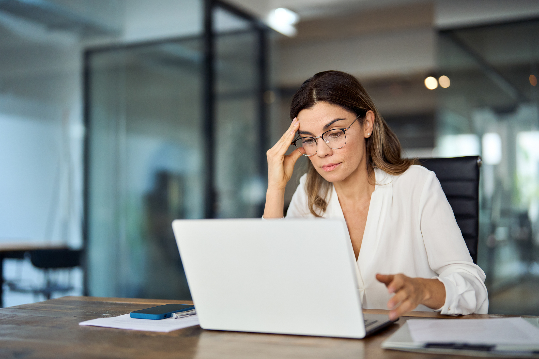 A mature business woman wearing glasses works at a laptop, weighing options for search-ads-vs-lsas-vs-pmax blog.