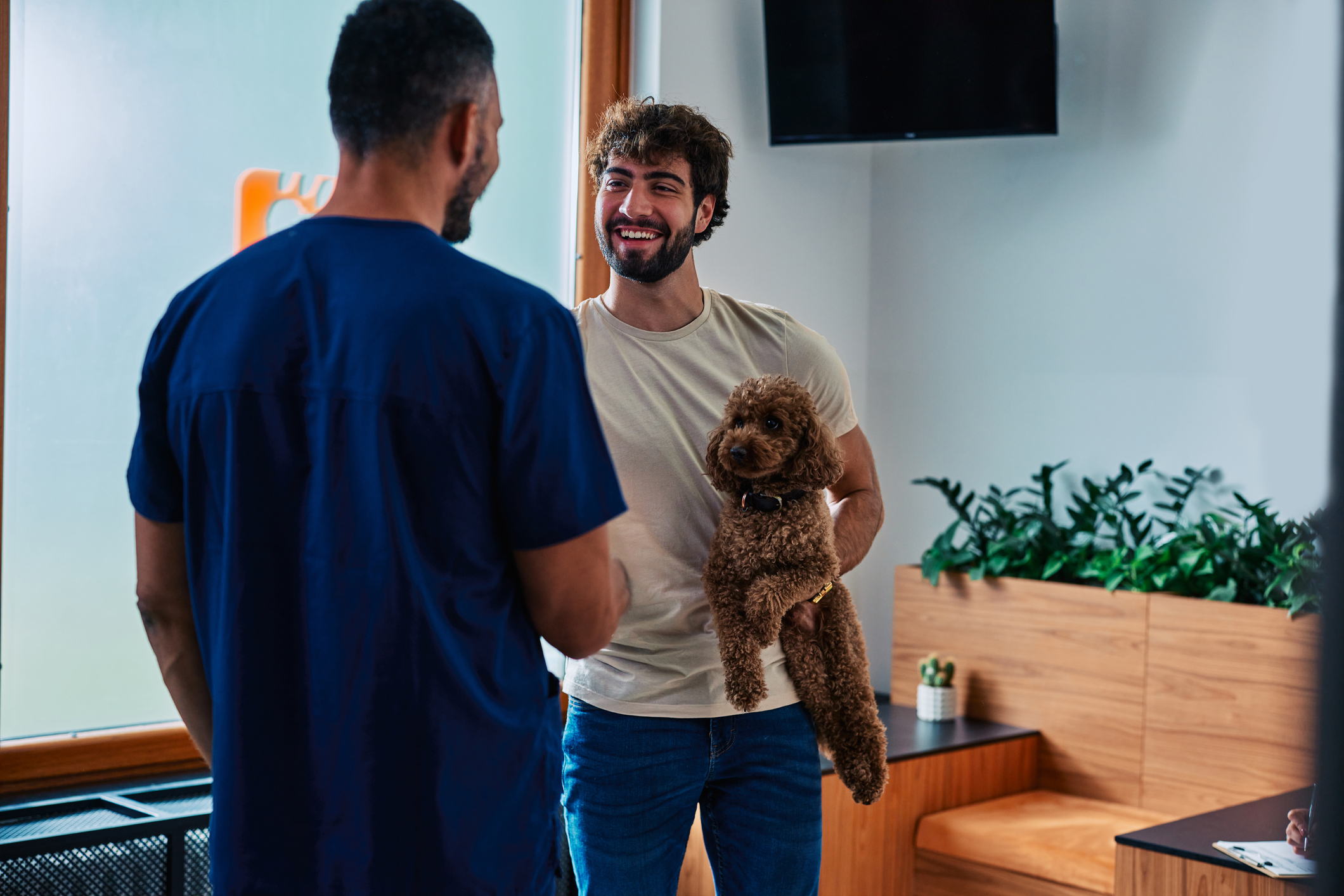 A man holding a brown poodle speaks with a pet care specialist at a facility for pet-care-differentiators blog.